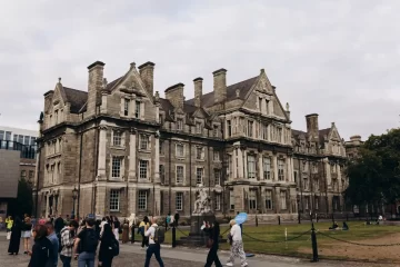 Prédio histórico na Irlanda, com fachada de pedra e grandes janelas, enquanto pessoas caminham pelo pátio, ideal para ilustrar Intercâmbio Irlanda: Guia Completo (Estudo e Trabalho).